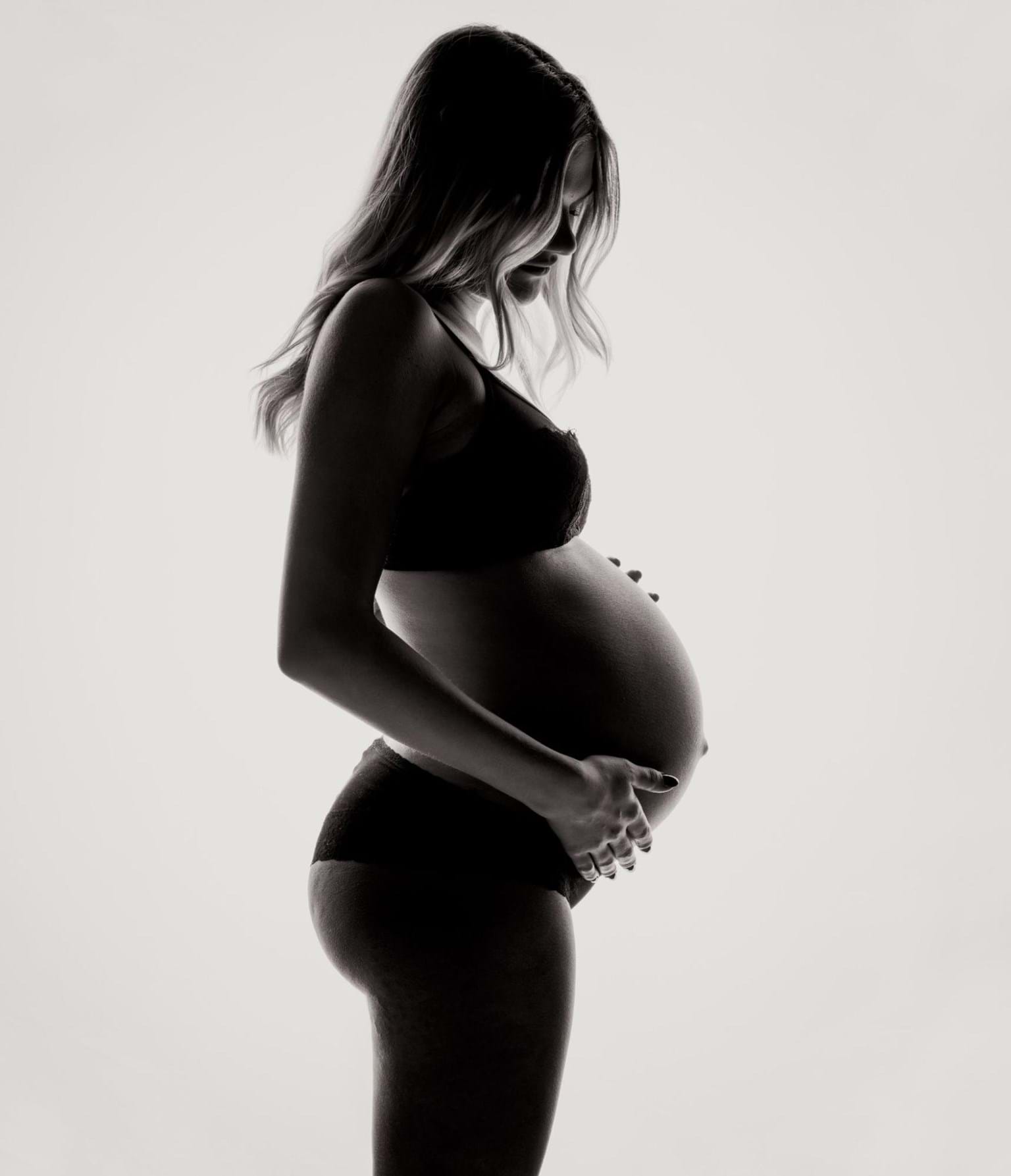 Pregnant woman in underwear holding belly, black and white profile, inspired by TCM.