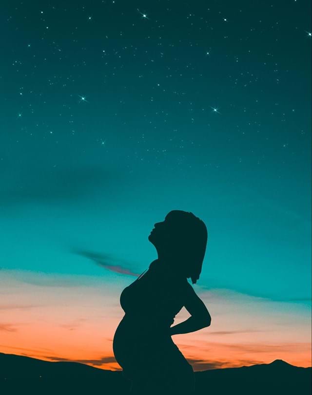 Silhouette of a pregnant woman at sunset, embracing acupuncture beneath a starry sky.