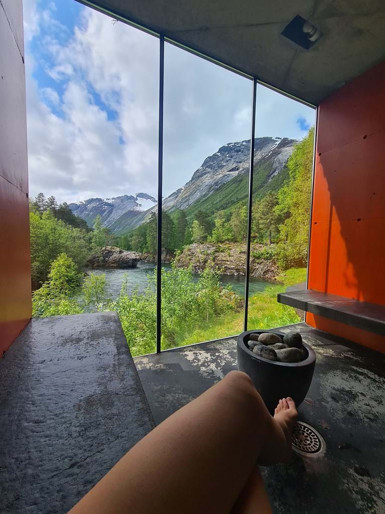 Person relaxing in modern room with large window, enjoying mountains, river, and acupuncture.