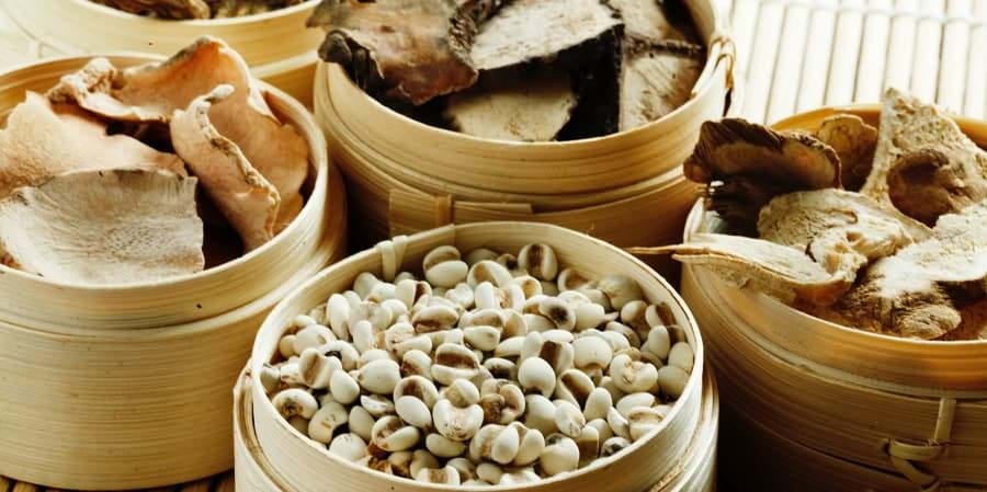 Round bamboo baskets of dried herbs and seeds, essentials in Chinese herbal medicine, on a mat.