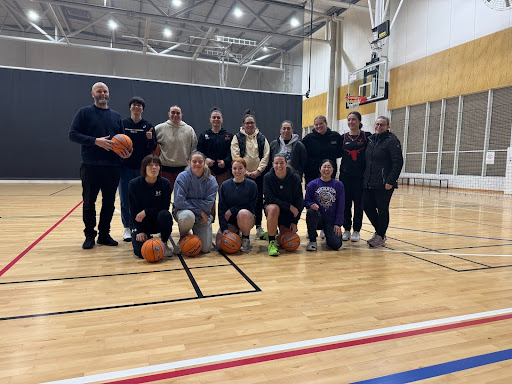 A group of people pose with basketballs on an indoor basketball court.