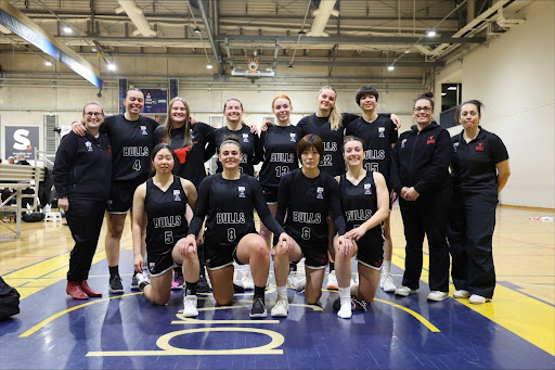 A women's basketball team poses together on an indoor court for a group photo.