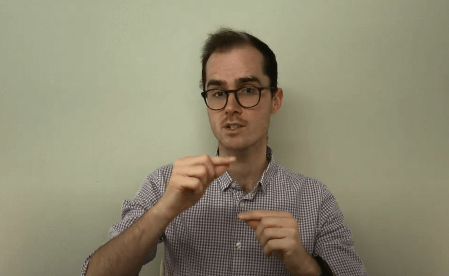 A person wearing glasses signs in front of a plain wall about acupuncture.